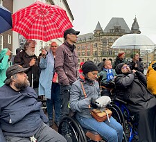 Im Regen findet eine Begehung des Domsheide statt. Die Teilnehmenden teils im Rollstuhl und mit Regenschirmen.